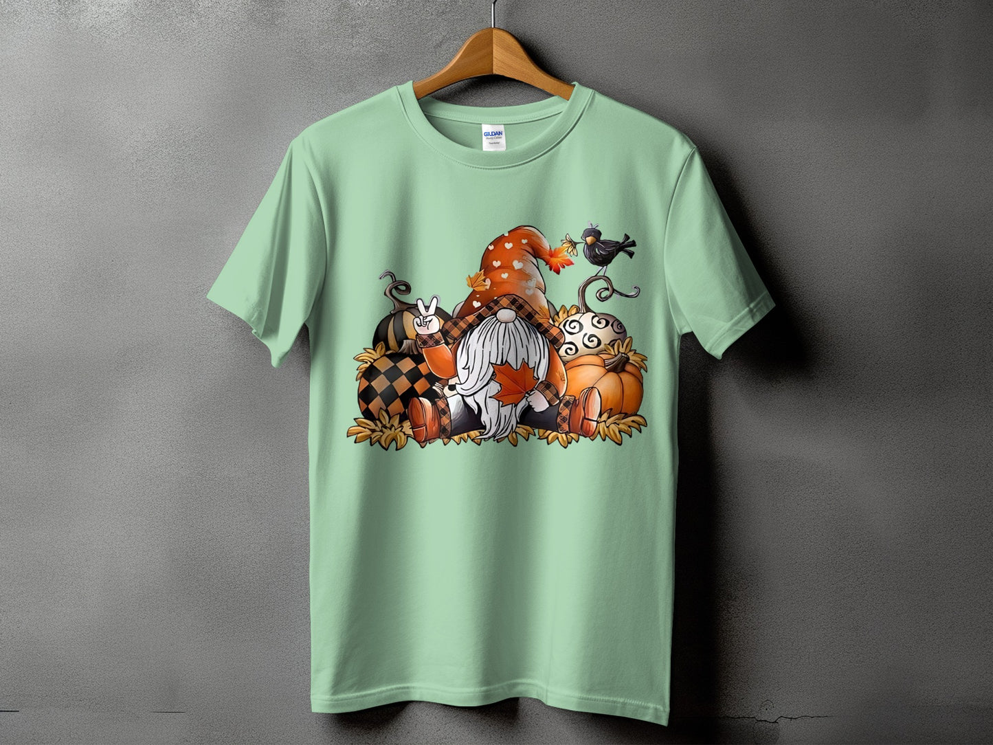 Gnome with pumpkins, leaves, and a crow on a light green t-shirt.