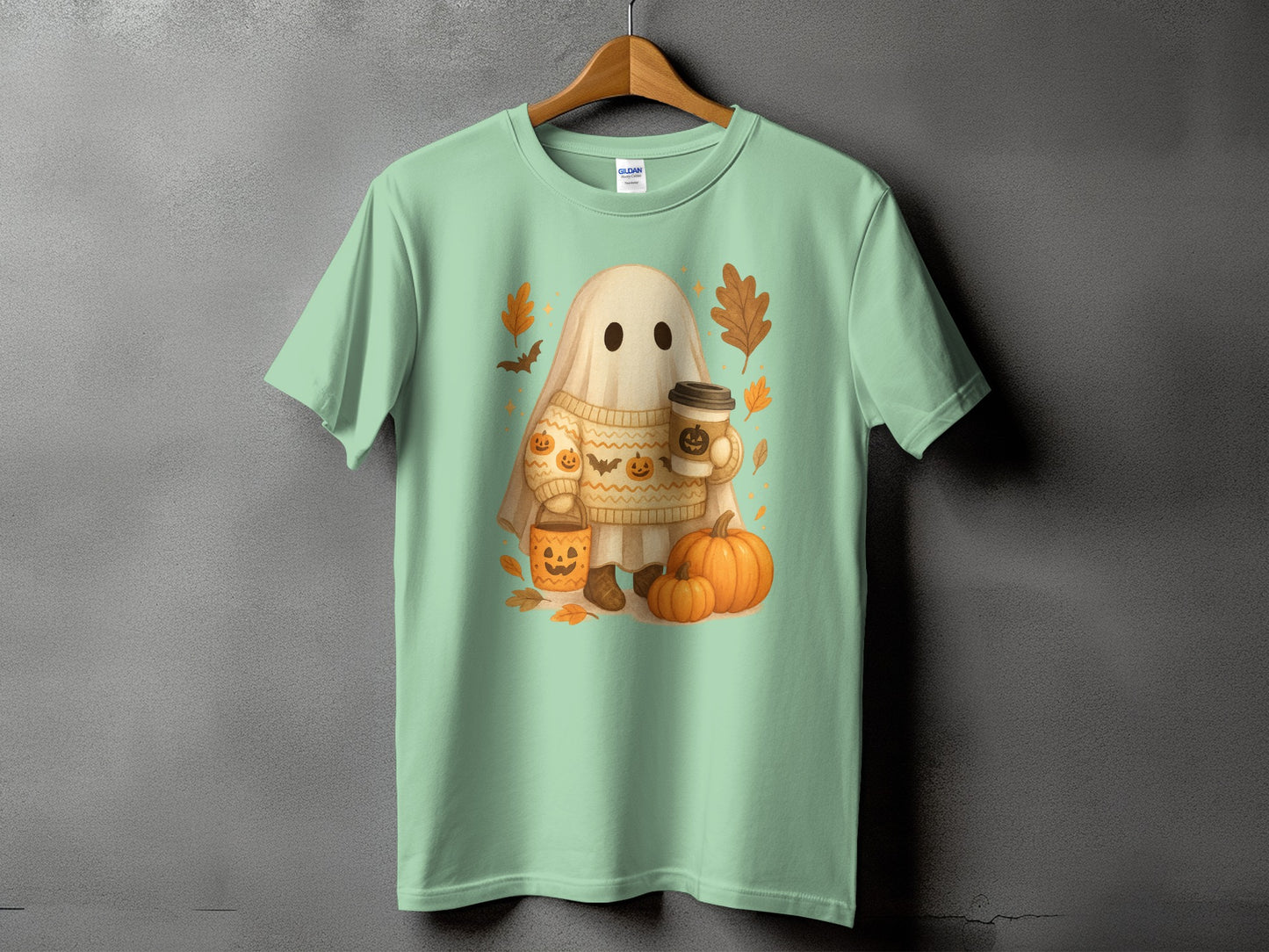Mint green t-shirt with a cartoon ghost holding a coffee cup and surrounded by pumpkins and leaves.