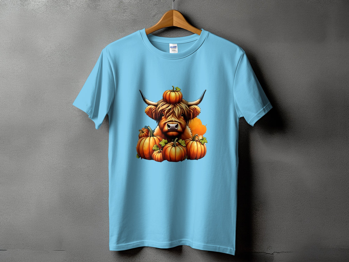 Light blue t-shirt featuring a Highland cow illustration with pumpkins.