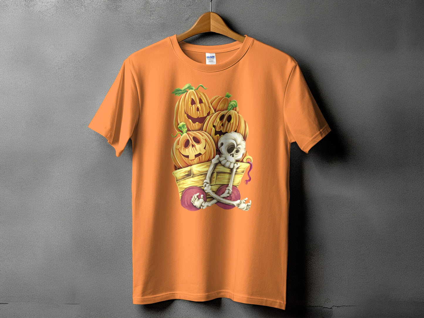 Orange t-shirt with a Halloween graphic of a skeleton and pumpkins in a wagon.