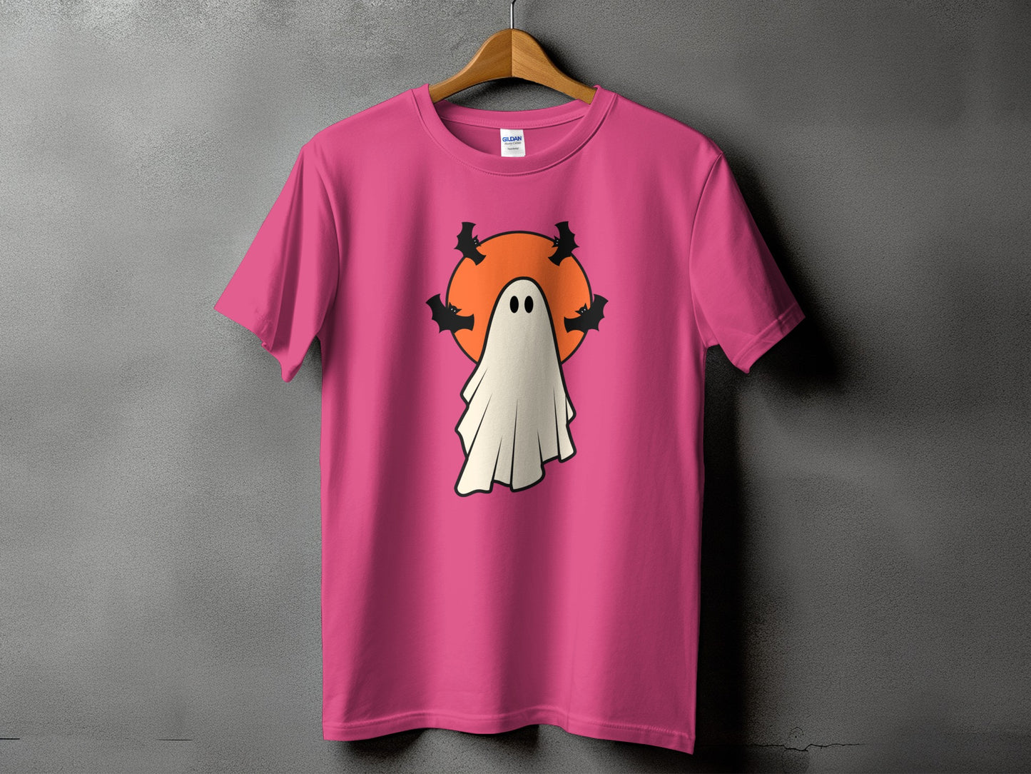 Pink t-shirt with a cartoon ghost and bats in front of an orange circle.
