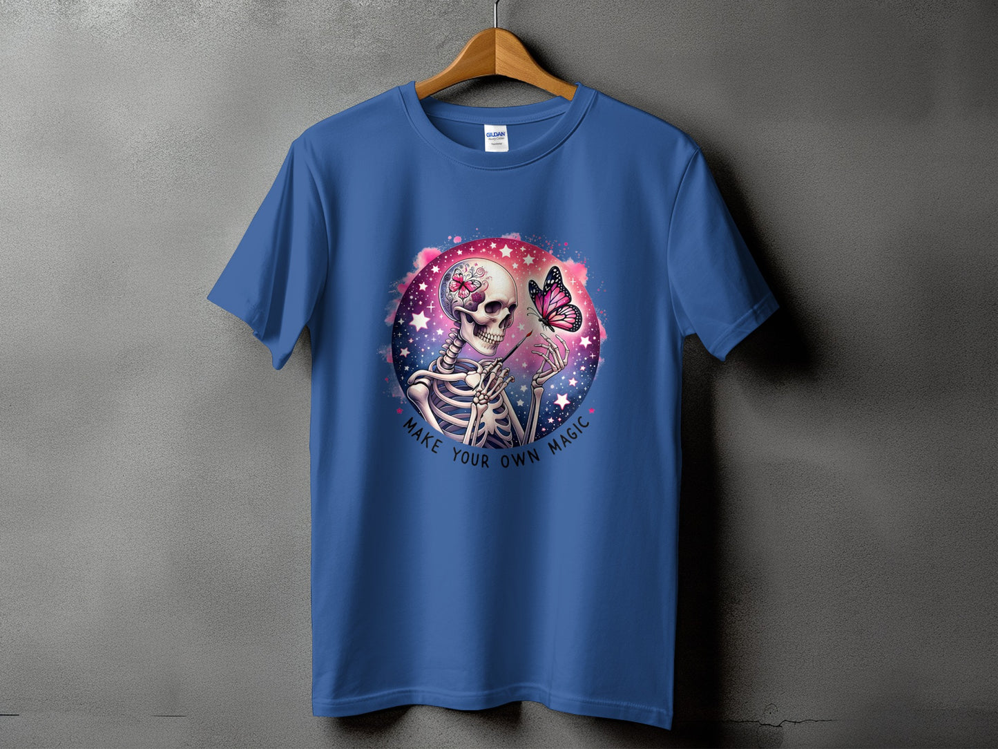 Blue t-shirt with skeleton graphic, butterfly, and text "MAKE YOUR OWN MAGIC."