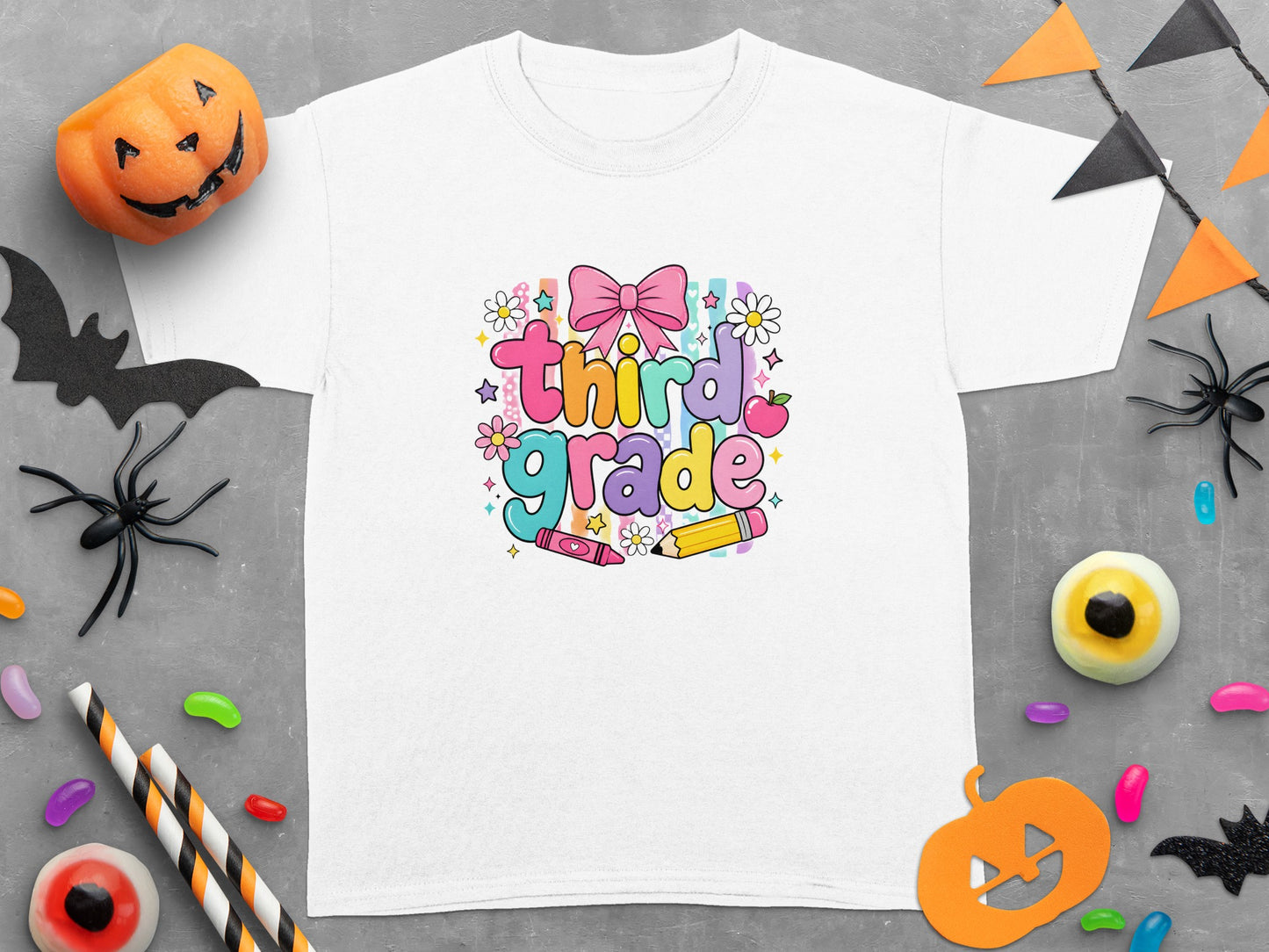 White t-shirt with colorful "third grade" text, bow, apple, and school supplies.