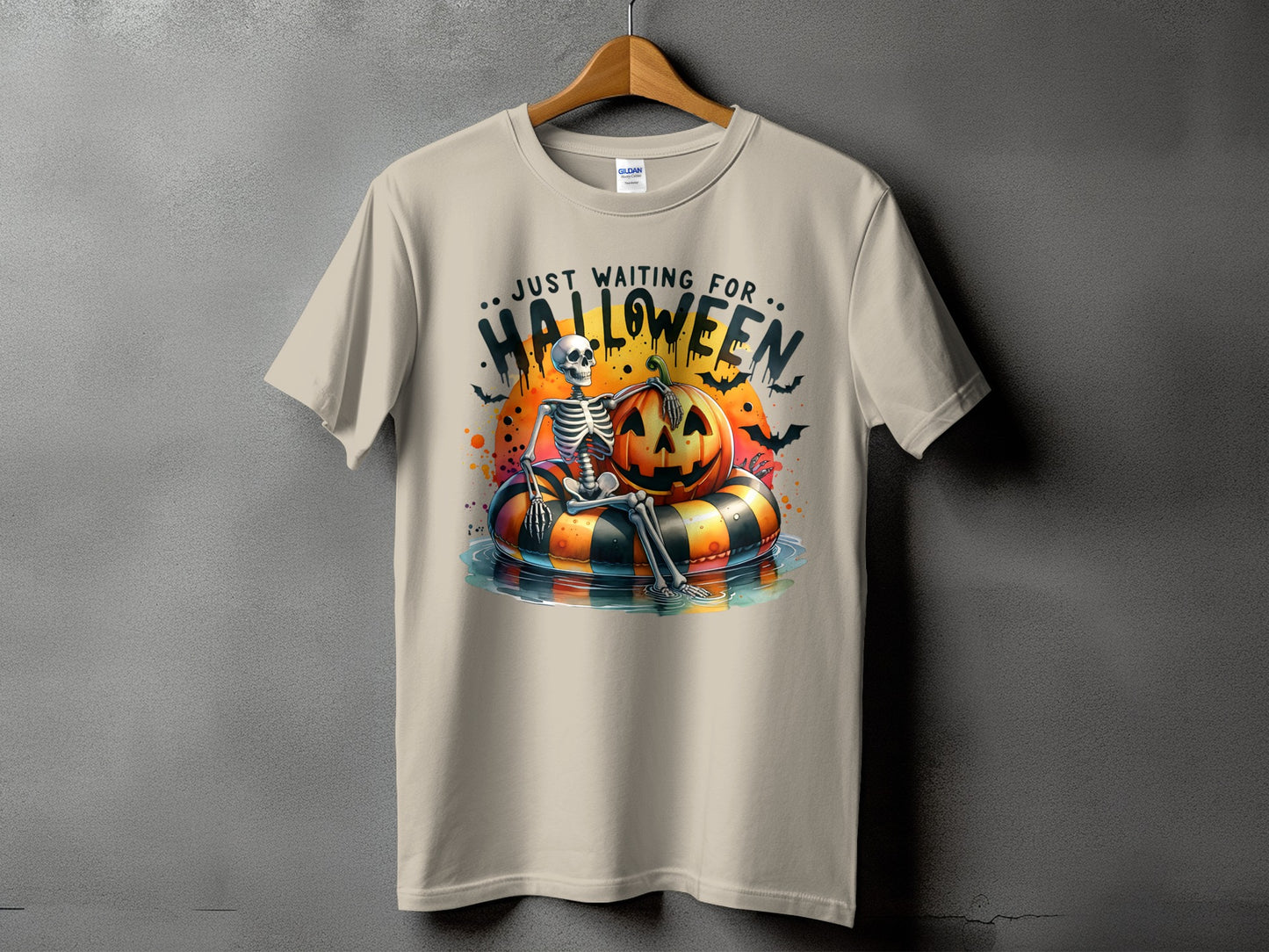 Skeleton on an inner tube with a pumpkin and bats, text reads "Just Waiting For Halloween".