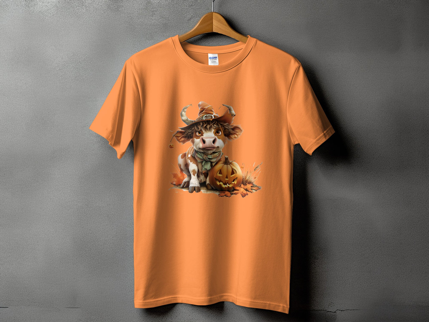 Orange t-shirt with a cartoon cow in a witch hat and pumpkin graphic.