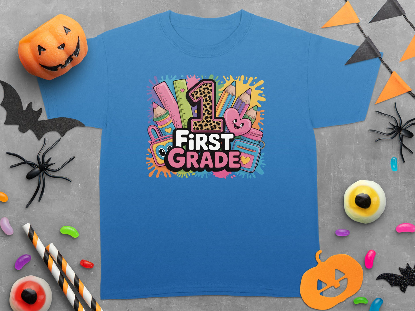 Blue t-shirt with "First Grade" text and school supplies graphic surrounded by Halloween decorations.
