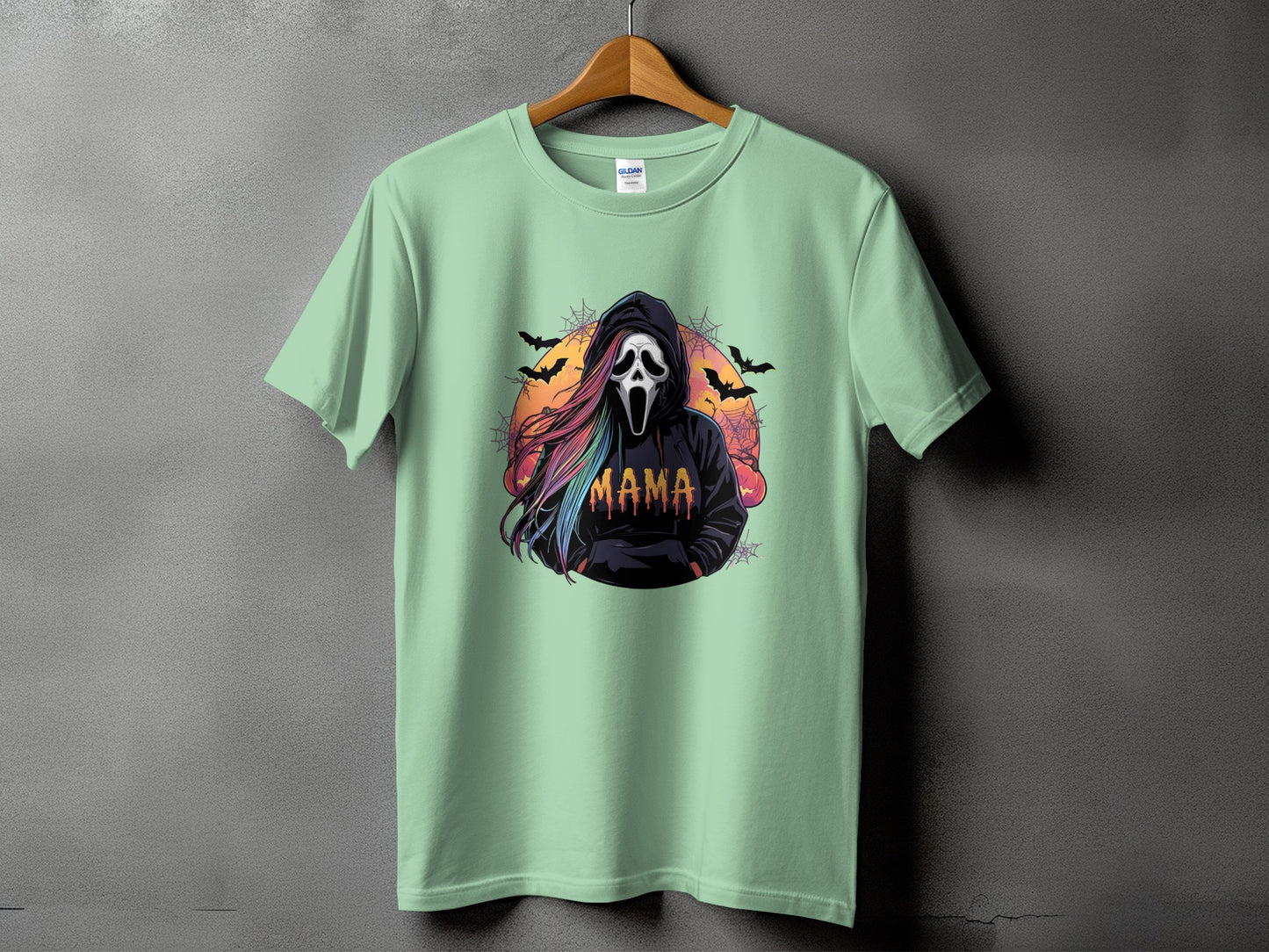 T-shirt with ghost face, rainbow hair, and "MAMA" text, set against bats and sunset.