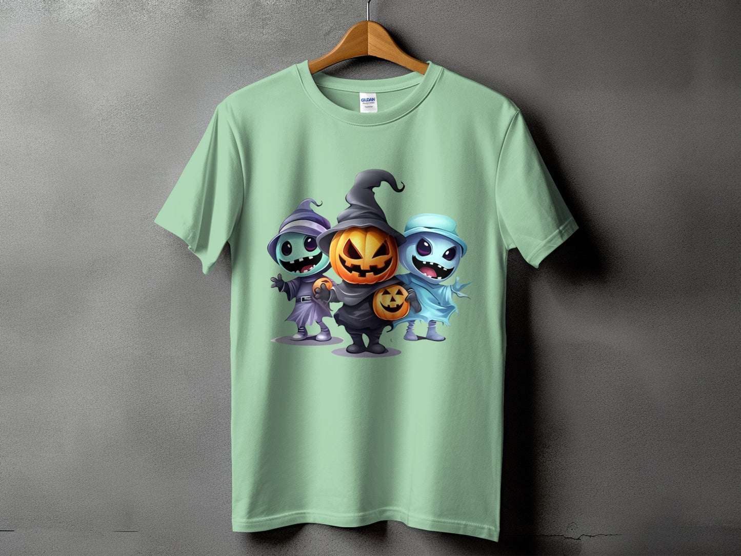 Light green t-shirt with three cartoon Halloween characters: witch, jack-o'-lantern, and ghost.