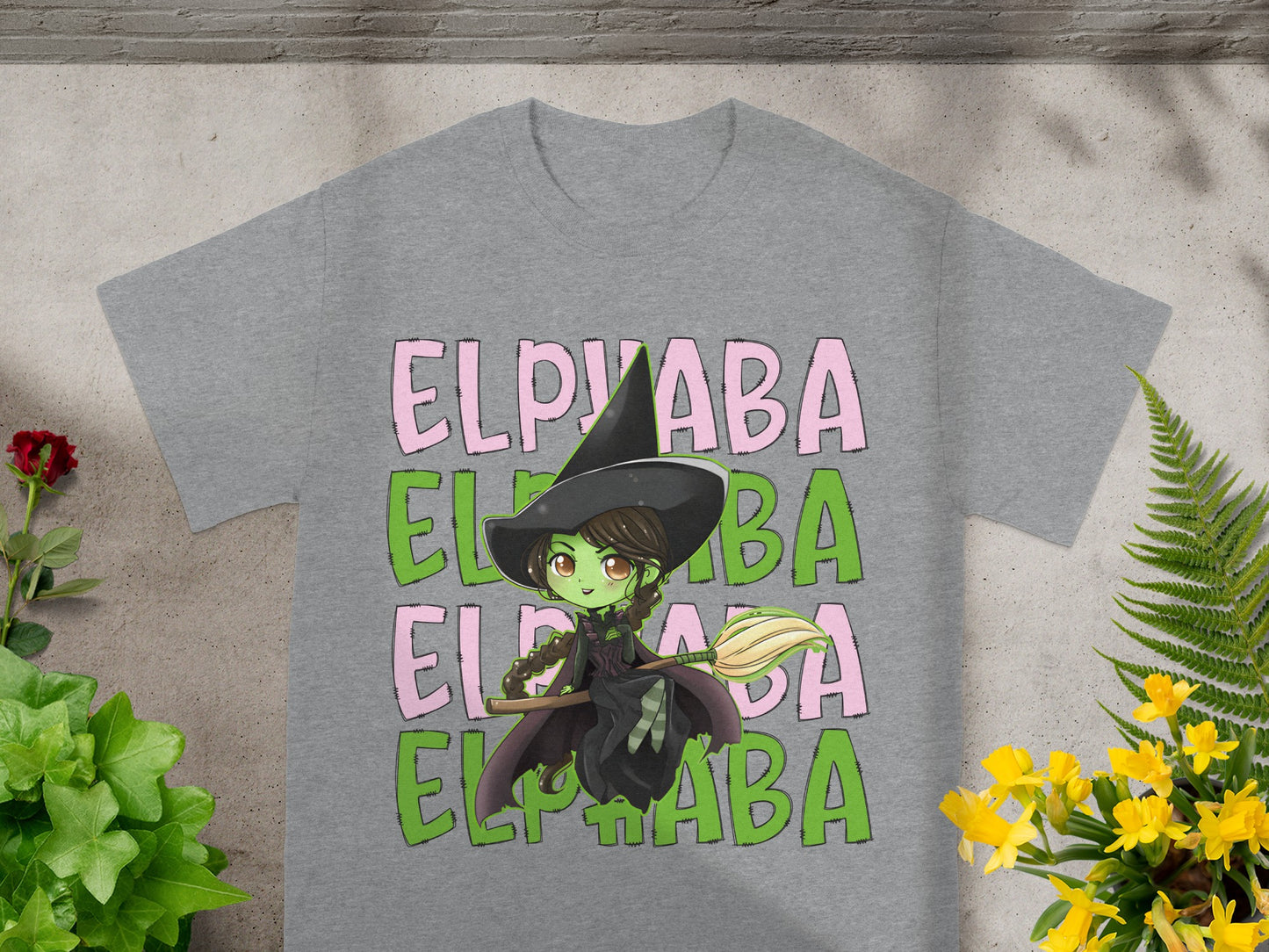 Green witch with broom on t-shirt, text reads "ELPHABA".