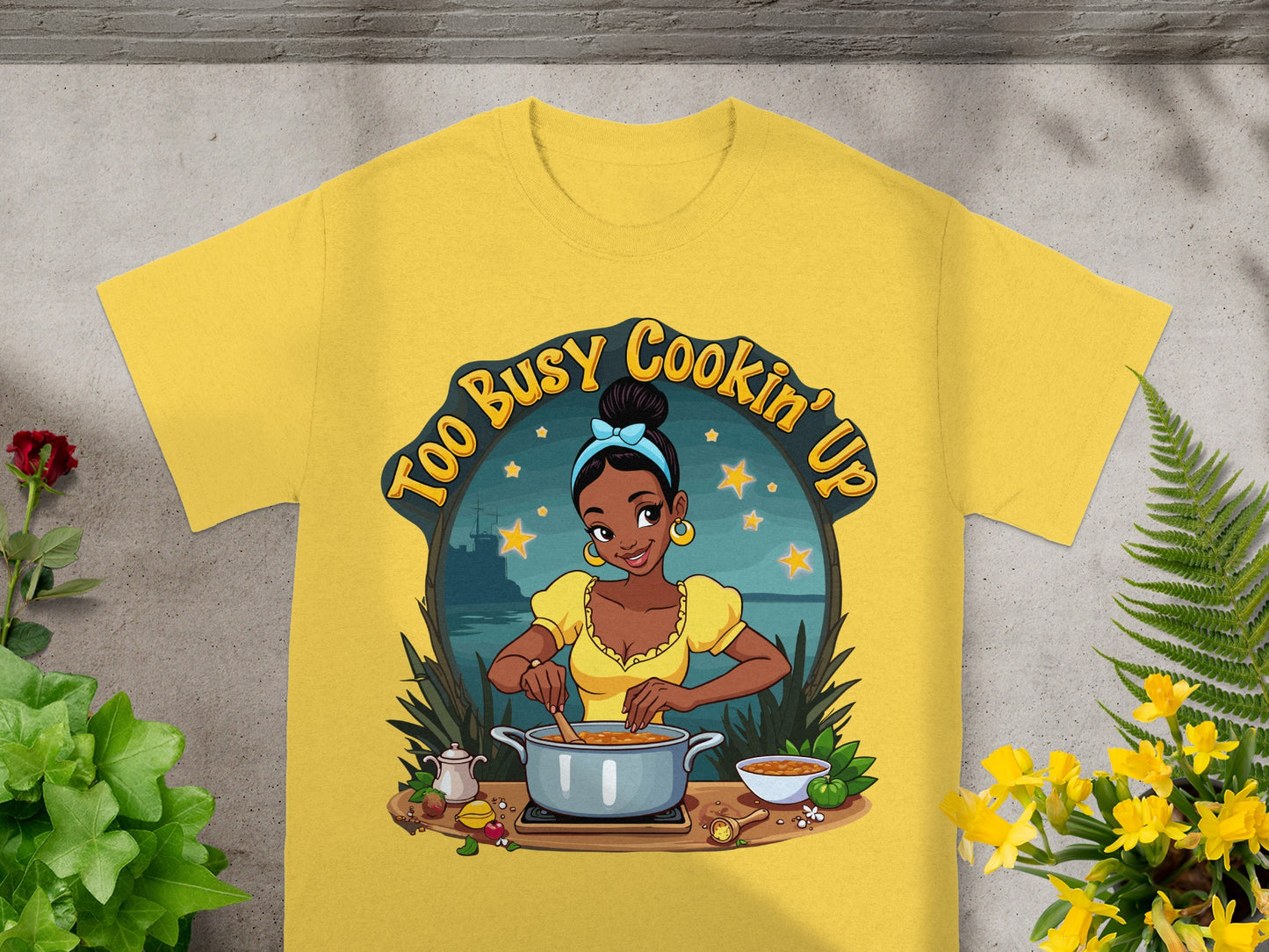 Yellow t-shirt with graphic of a Black woman cooking, "Too Busy Cookin' Up" text.