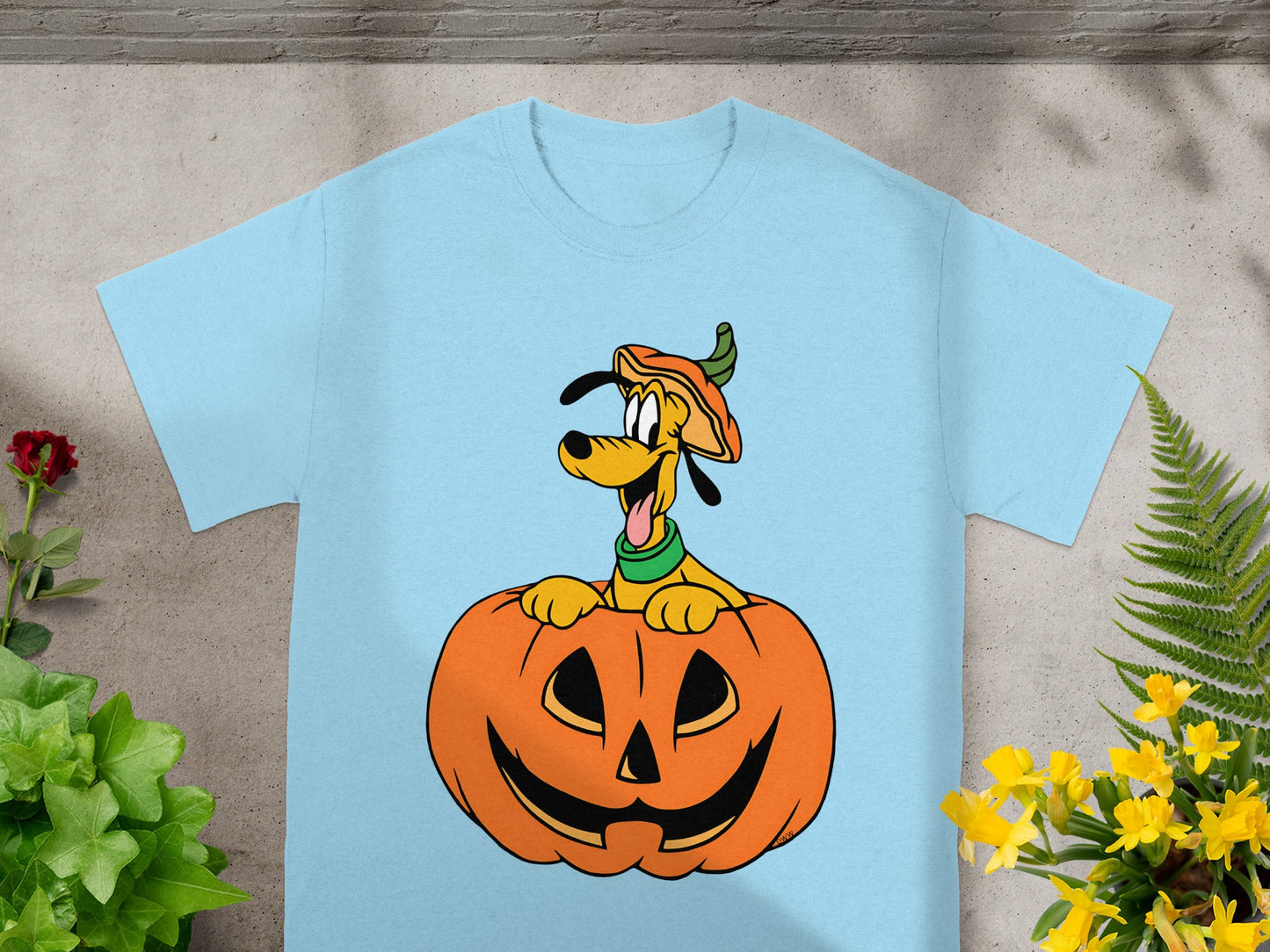 Pluto wearing a pumpkin hat peeking out of a jack-o'-lantern on a light blue t-shirt.