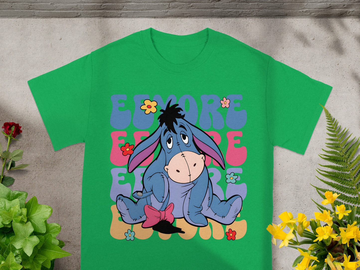 Eeyore sitting with "Eeyore" text and flowers on a green t-shirt.