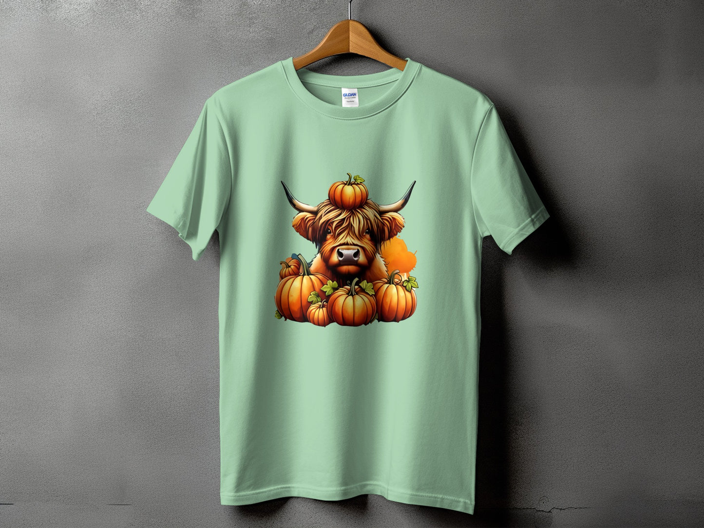 Light green t-shirt with a cow wearing a pumpkin on its head and surrounded by pumpkins.