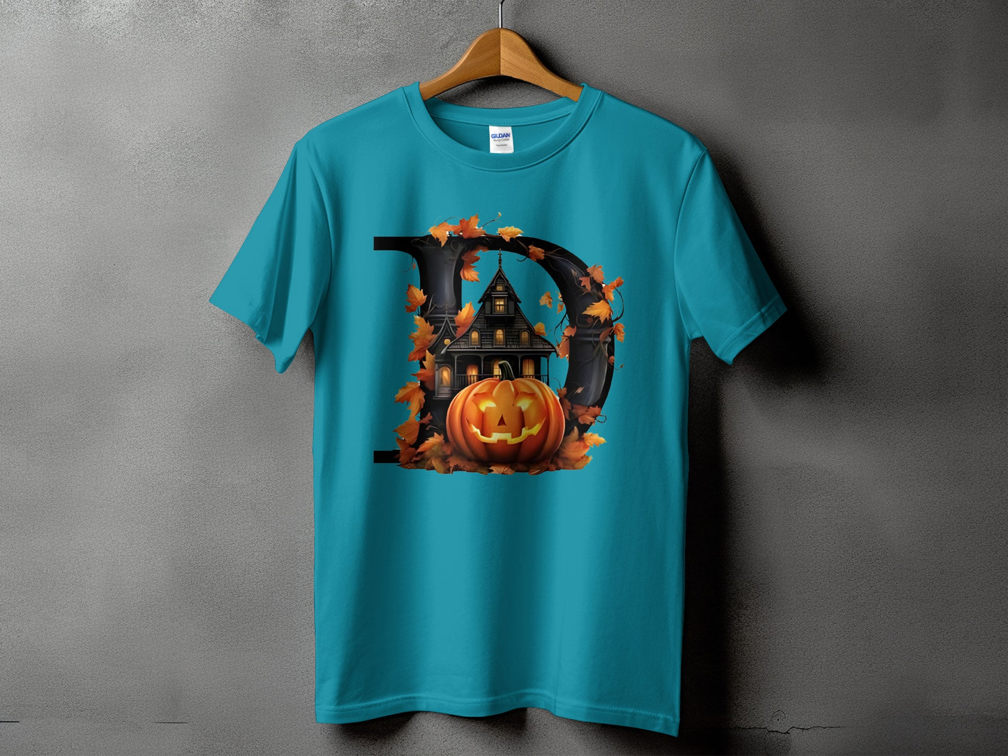 Teal t-shirt with a large black "D" shape framing a haunted house, pumpkin, and autumn leaves.