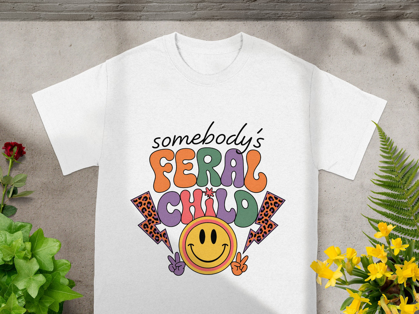 White t-shirt with "somebody's FERAL CHILD" graphic featuring smiley face and lightning bolts.