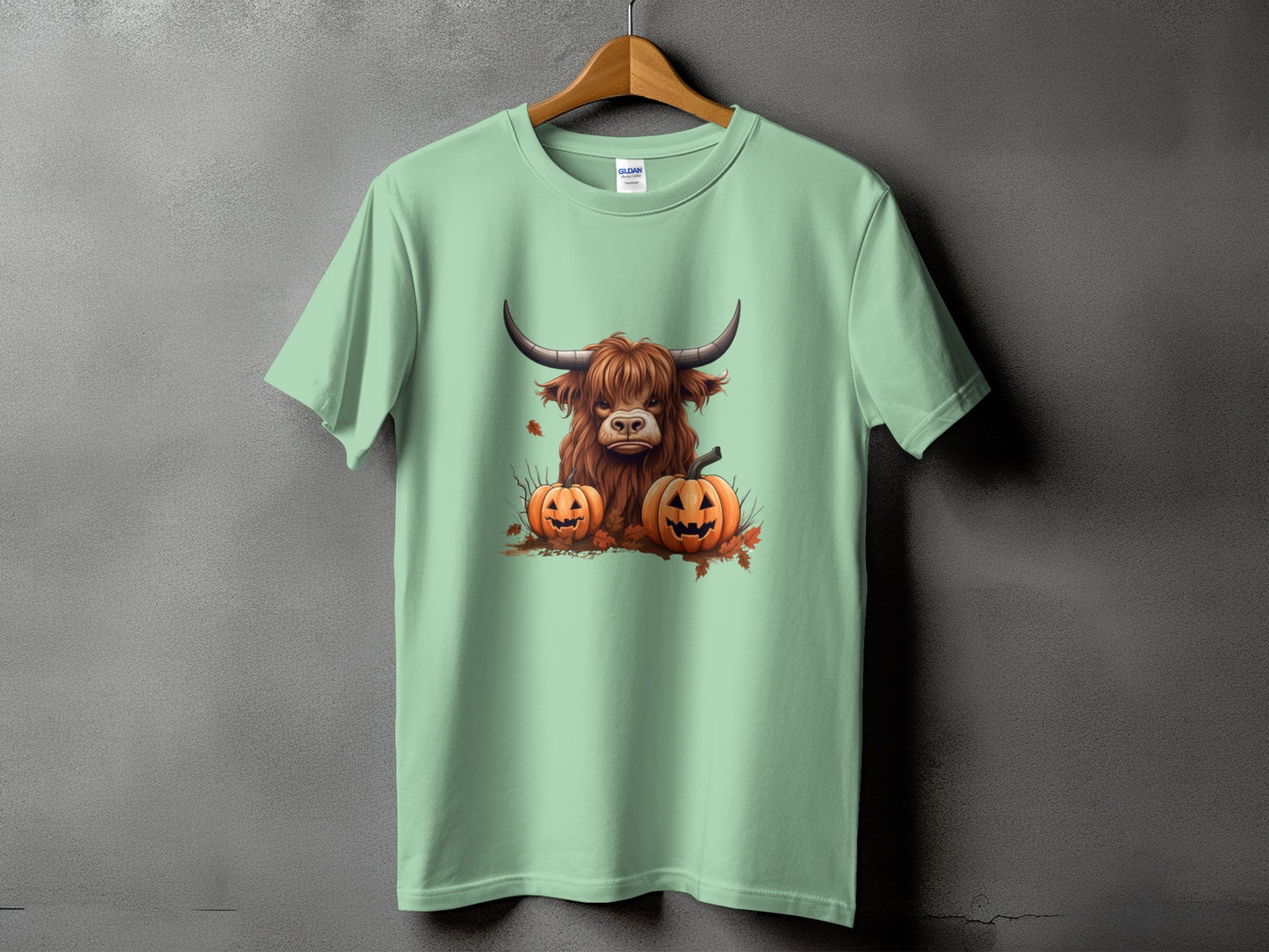 Highland cow and pumpkins graphic on a light green t-shirt.