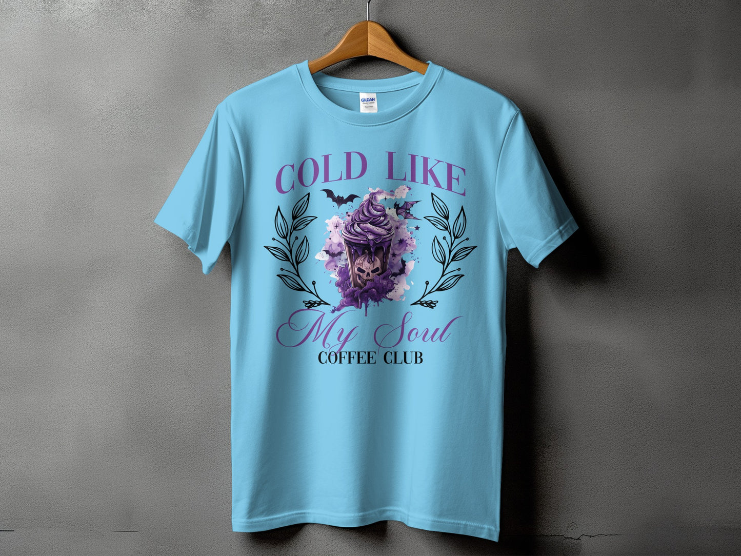 Light blue t-shirt with "COLD LIKE My Soul COFFEE CLUB" text and a spooky latte design.