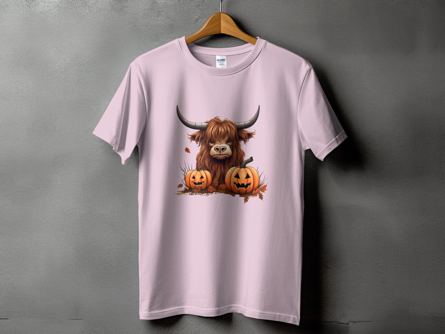 Pink t-shirt with a graphic of a Highland cow and two jack-o'-lanterns.