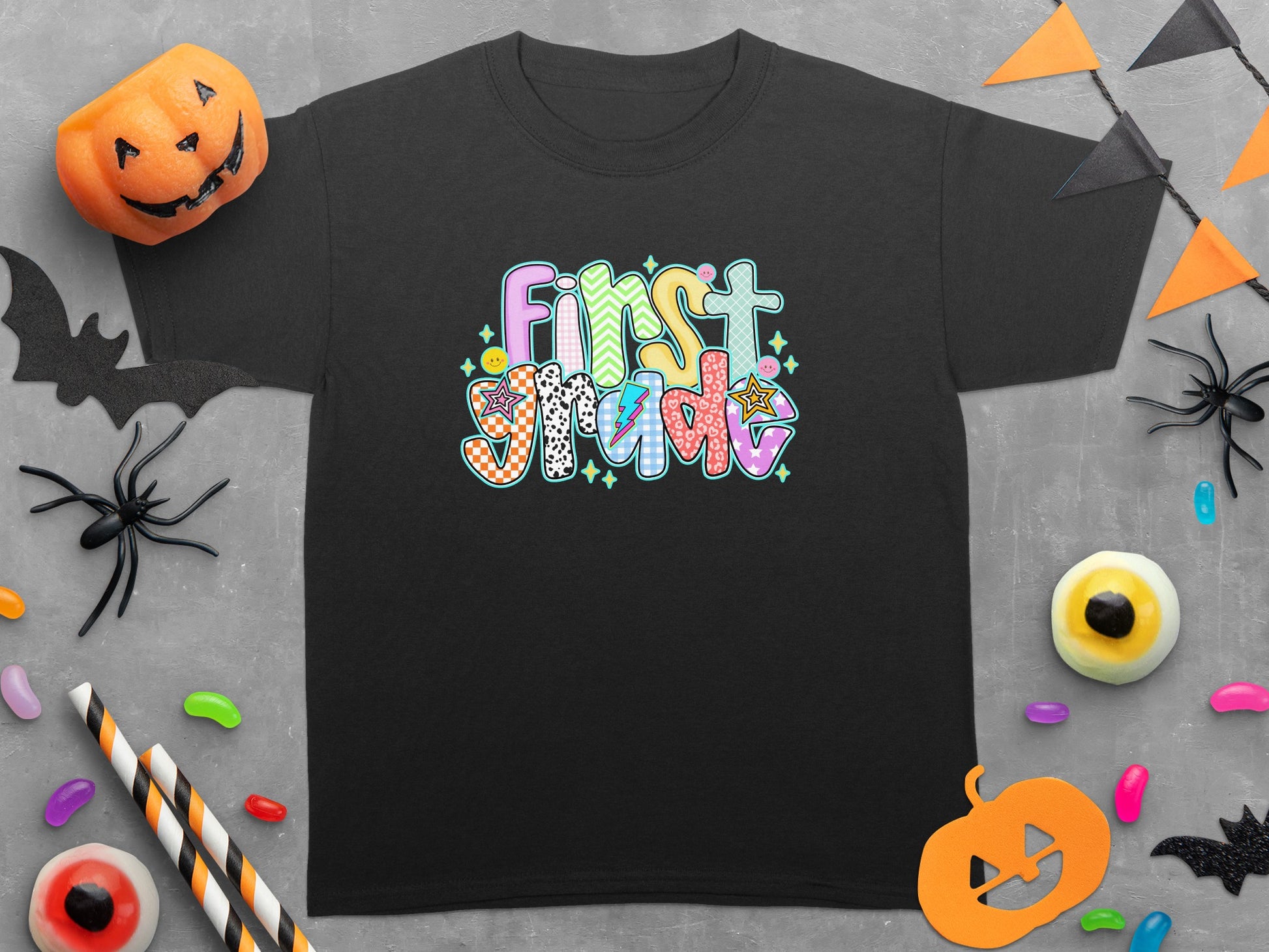 Black t-shirt with colorful "First Grade" text and Halloween decorations.