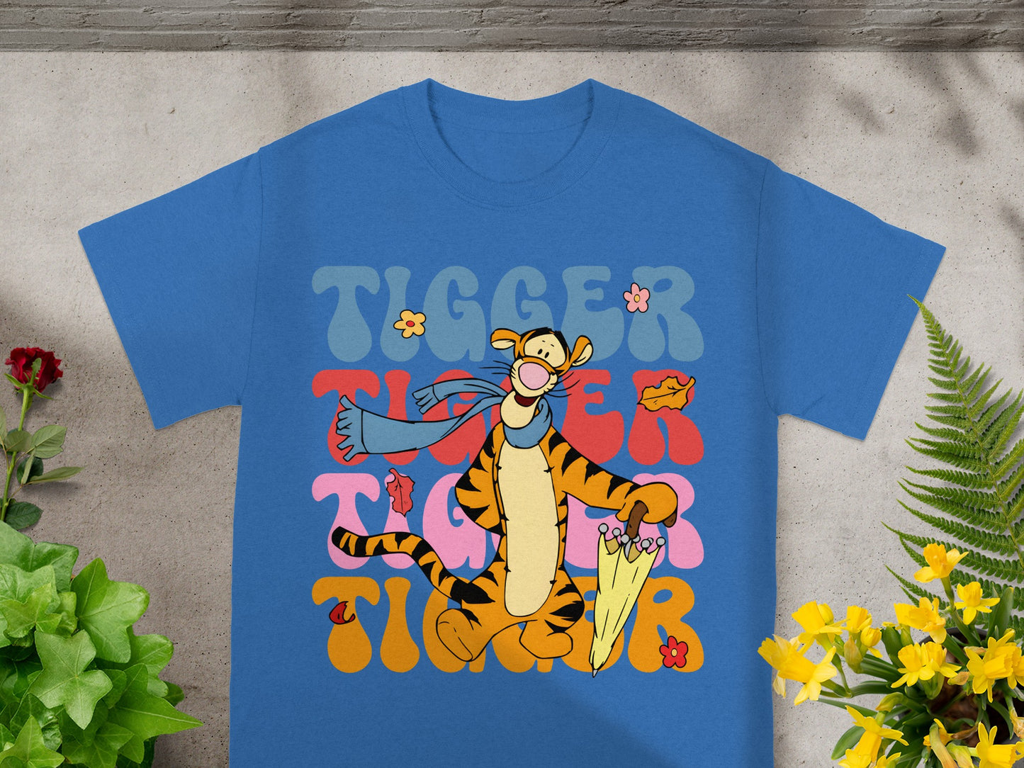 Tigger cartoon character wearing a scarf and holding an umbrella on a blue t-shirt.
