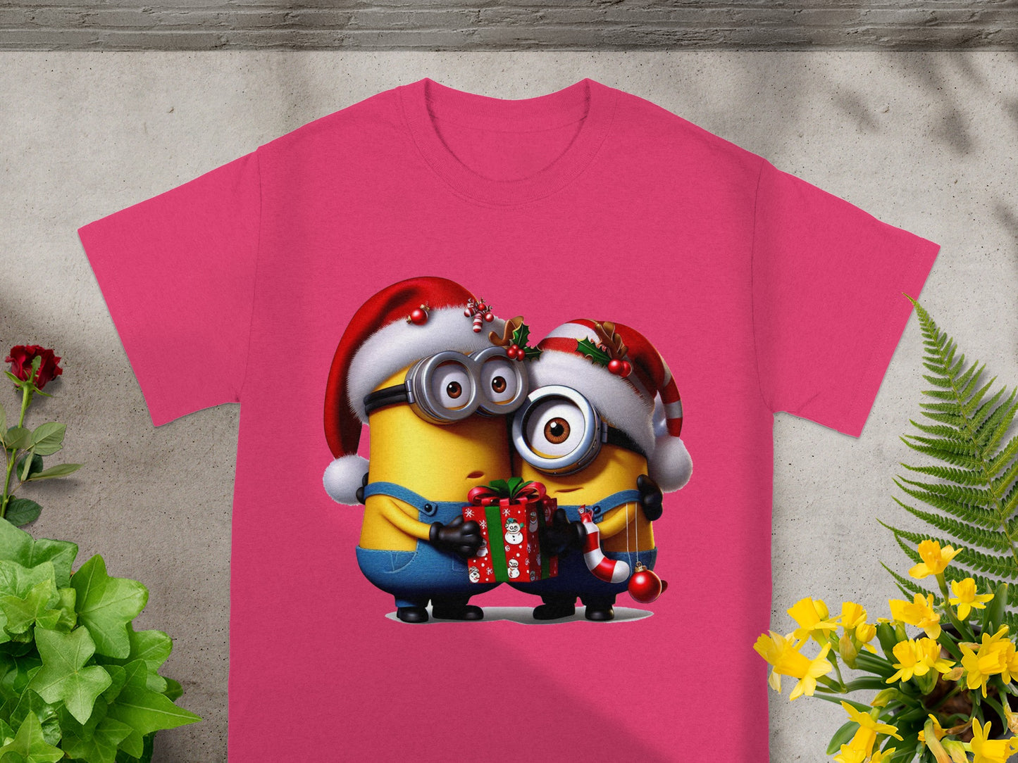 Two Minions in Santa hats hold a gift and candy cane on a pink t-shirt.