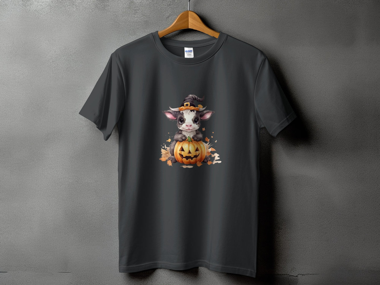 Dark grey t-shirt with a cartoon cow wearing a witch hat on a pumpkin.