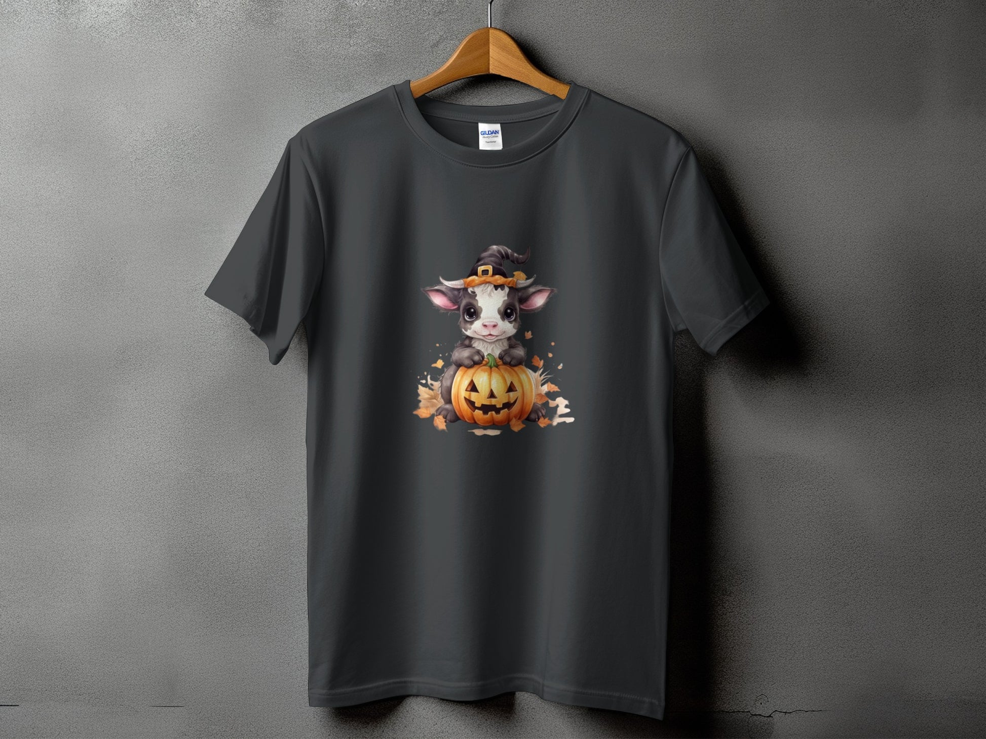 Dark grey t-shirt with a cartoon cow wearing a witch hat on a pumpkin.