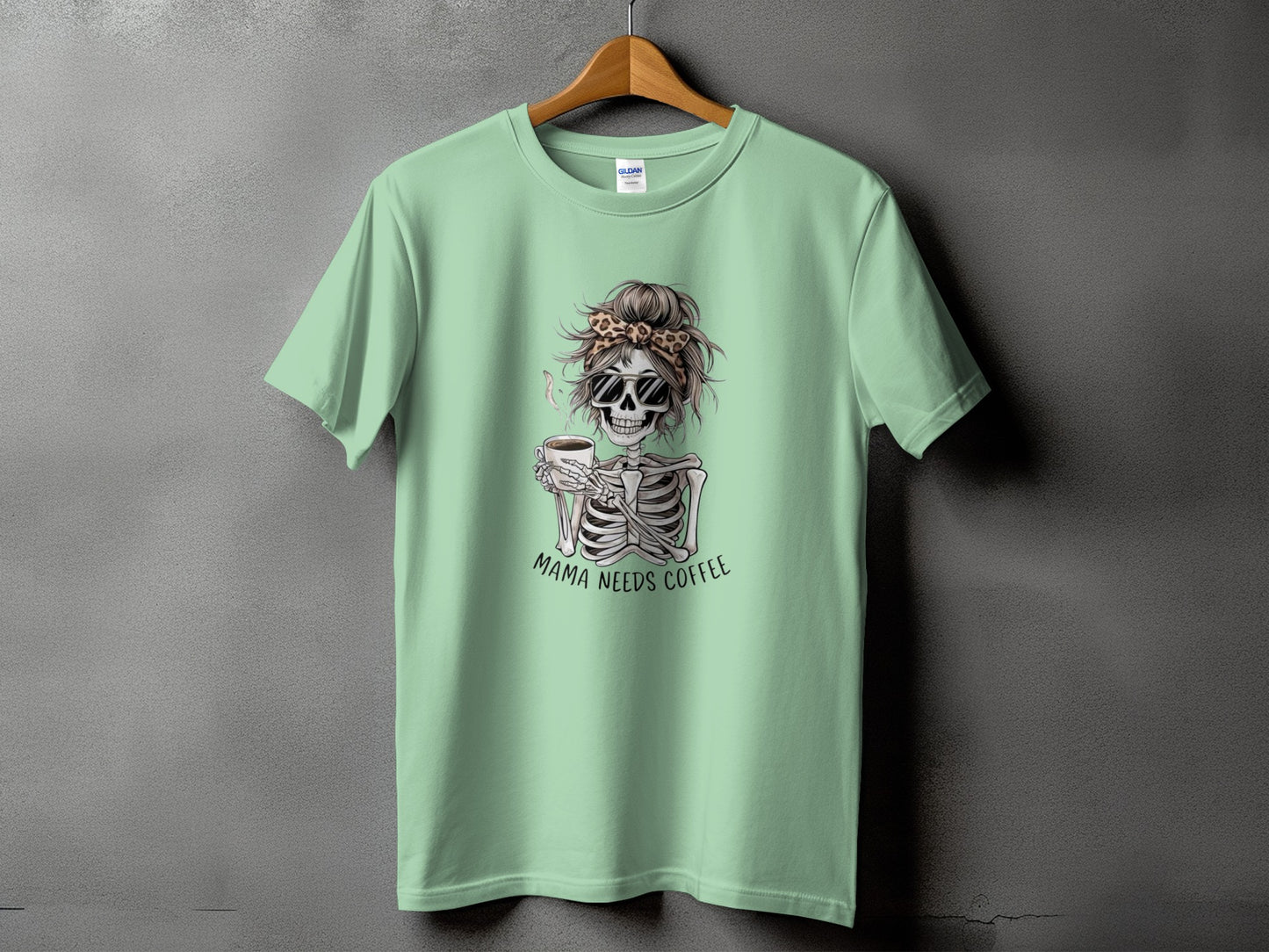 Light green t-shirt with skeleton graphic holding coffee and text "Mama Needs Coffee".
