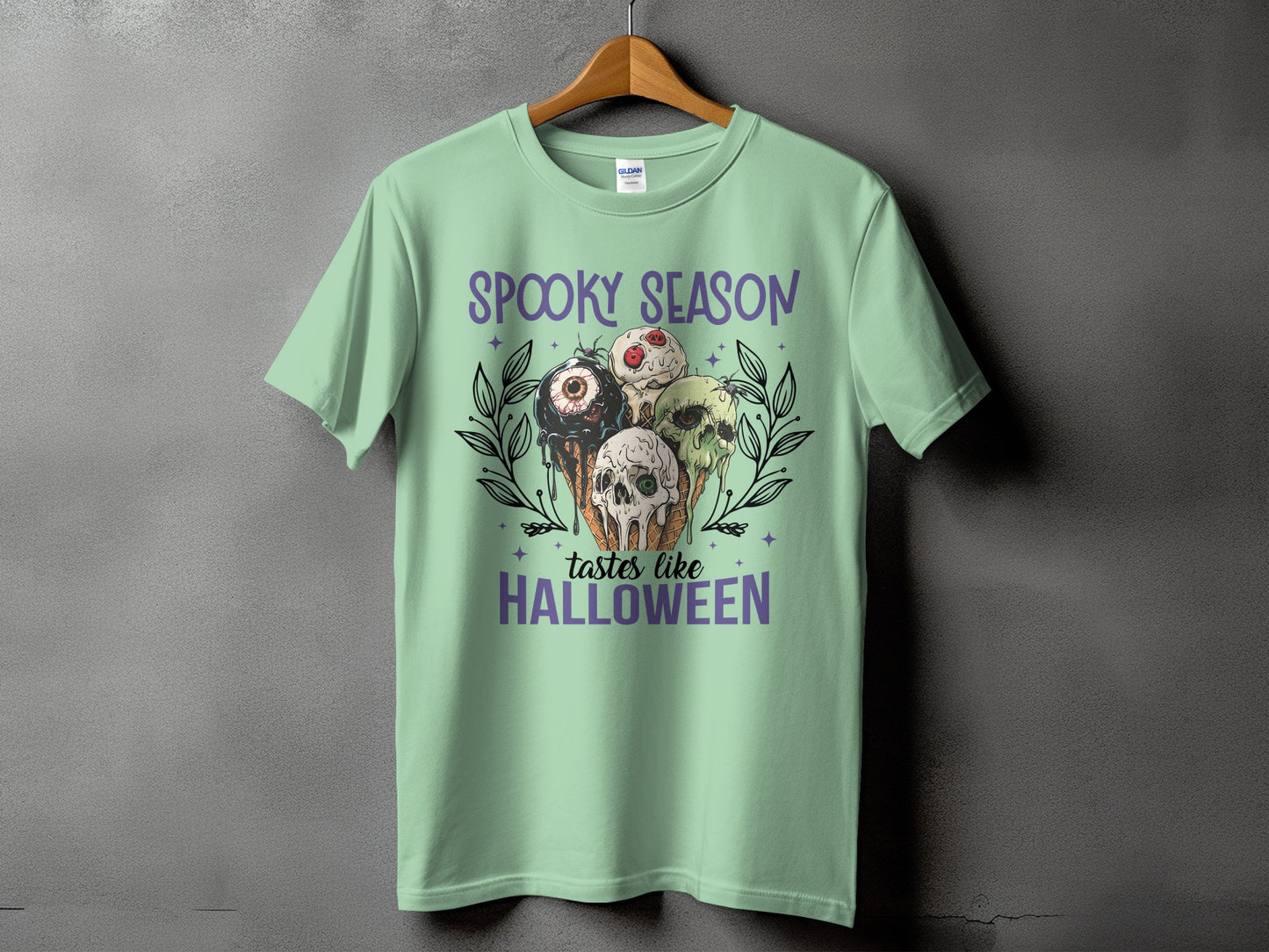 Light green t-shirt with "Spooky Season tastes like Halloween" and skull ice cream cones.