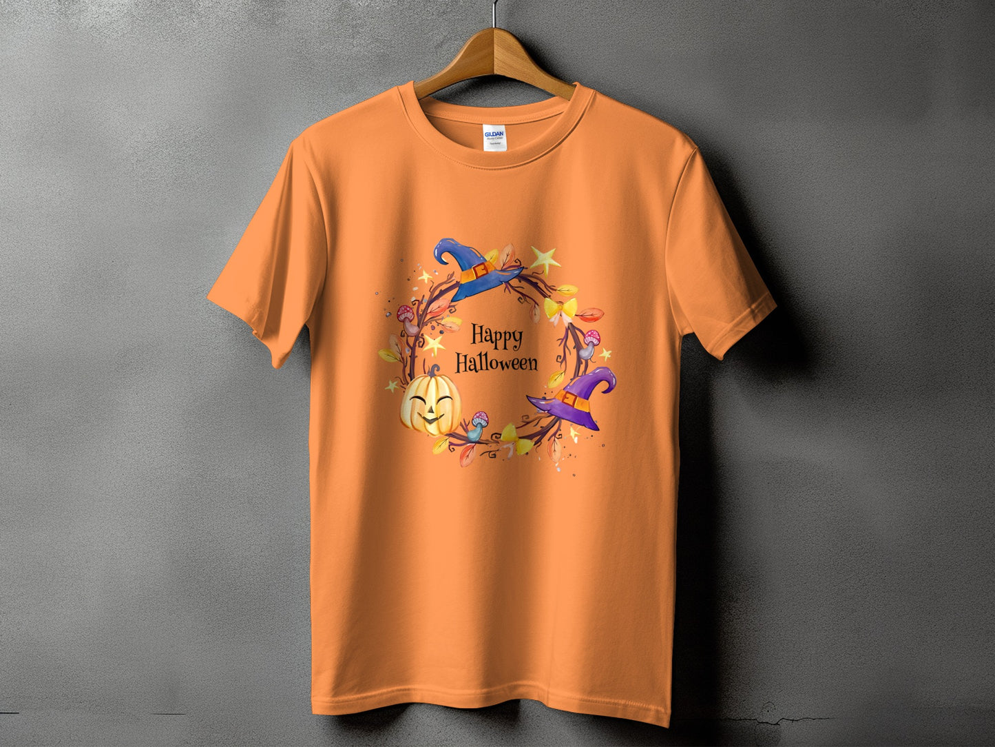 Orange t-shirt with a Halloween wreath graphic featuring a pumpkin and witch hats.