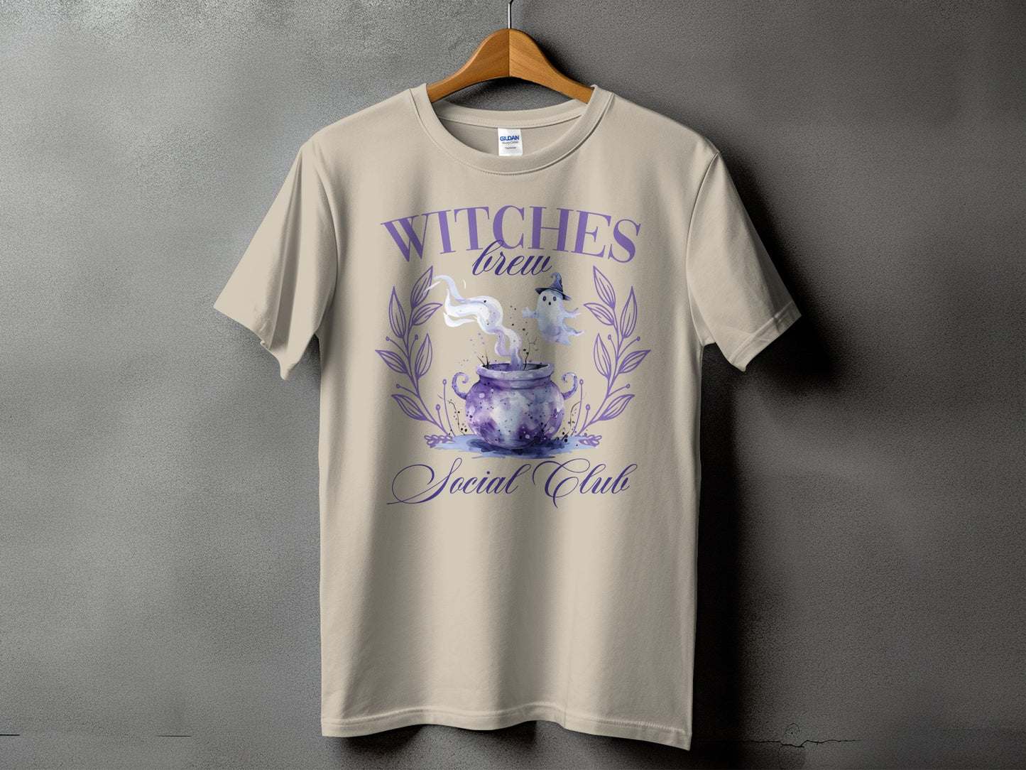 Witches Brew Social Club text with a cauldron and ghost graphic on a tan t-shirt.