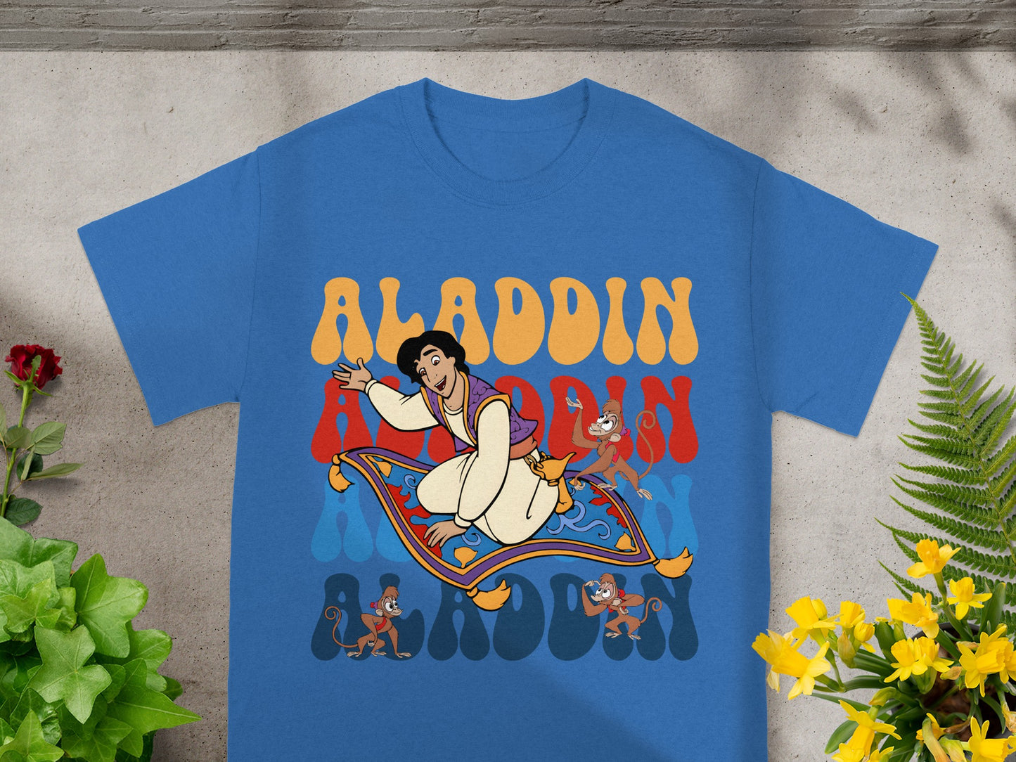 Blue t-shirt with Aladdin, Abu, and Genie graphic on a magic carpet.