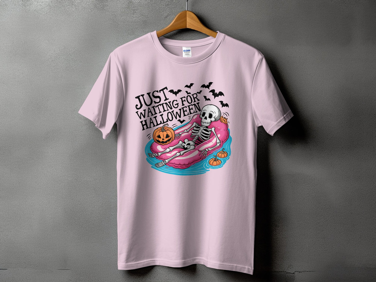 Skeleton floating on pink tube with pumpkin, bats, and text "JUST WAITING FOR HALLOWEEN".