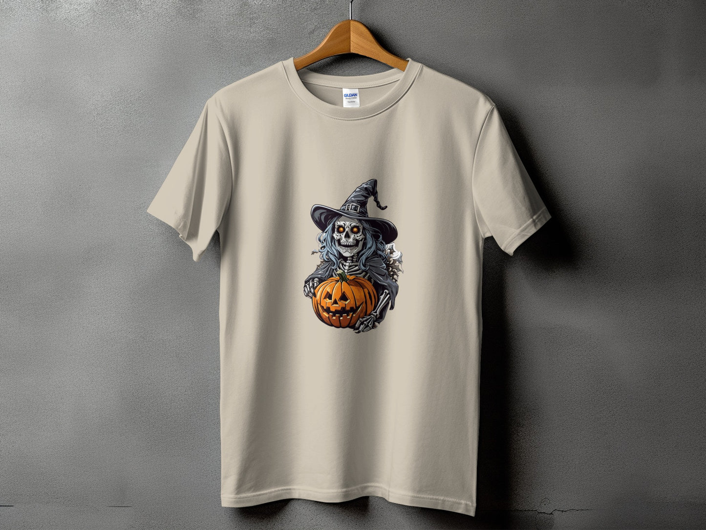 Skeleton in witch hat holding a carved pumpkin on a tan t-shirt.