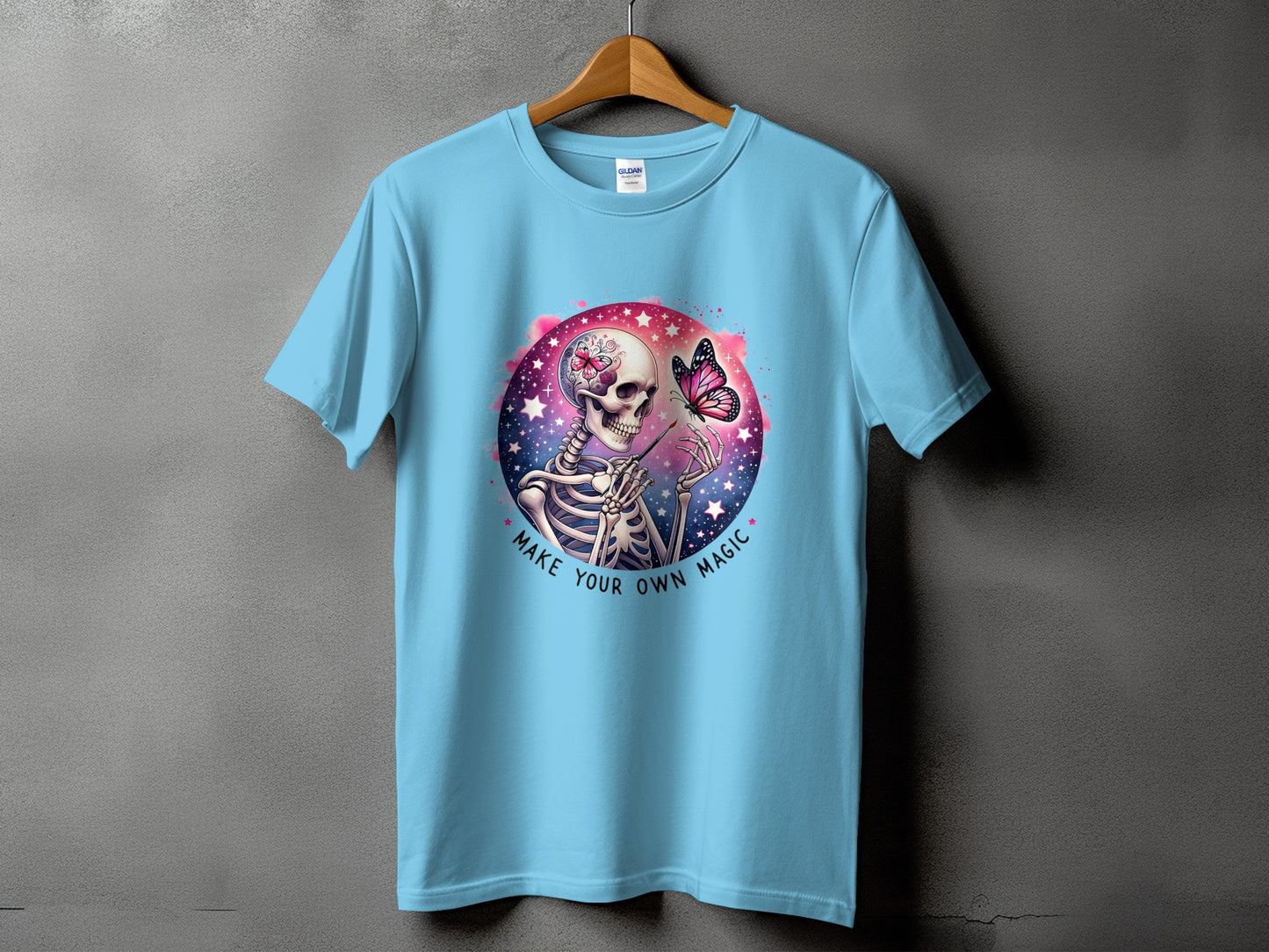 Light blue t-shirt with a skeleton, butterfly, and text "MAKE YOUR OWN MAGIC" graphic.