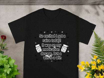 Black t-shirt with text: "So excited I got a raise today! It was on my medication dosage, but a win is a win".