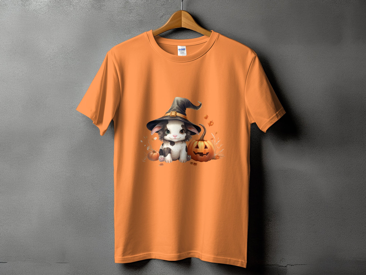 Orange t-shirt with a cute cow wearing a witch hat beside a jack-o'-lantern.