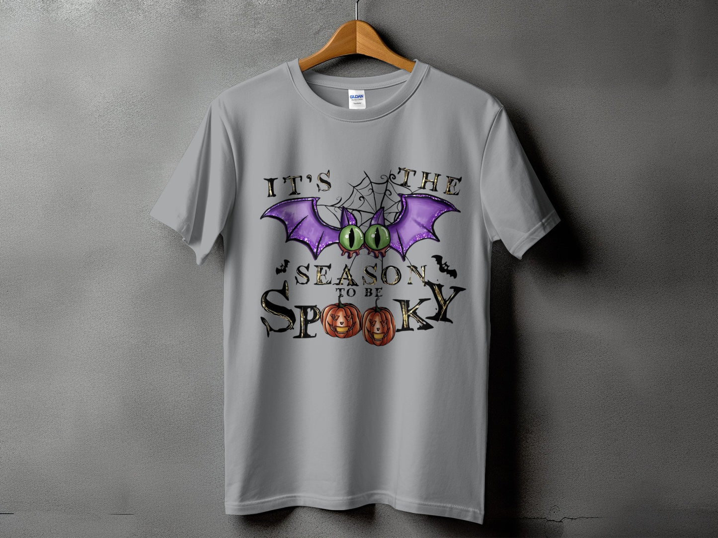Gray t-shirt with a Halloween graphic featuring a bat, spiderweb, pumpkins, and text "IT'S THE SEASON TO BE SPOOKY."