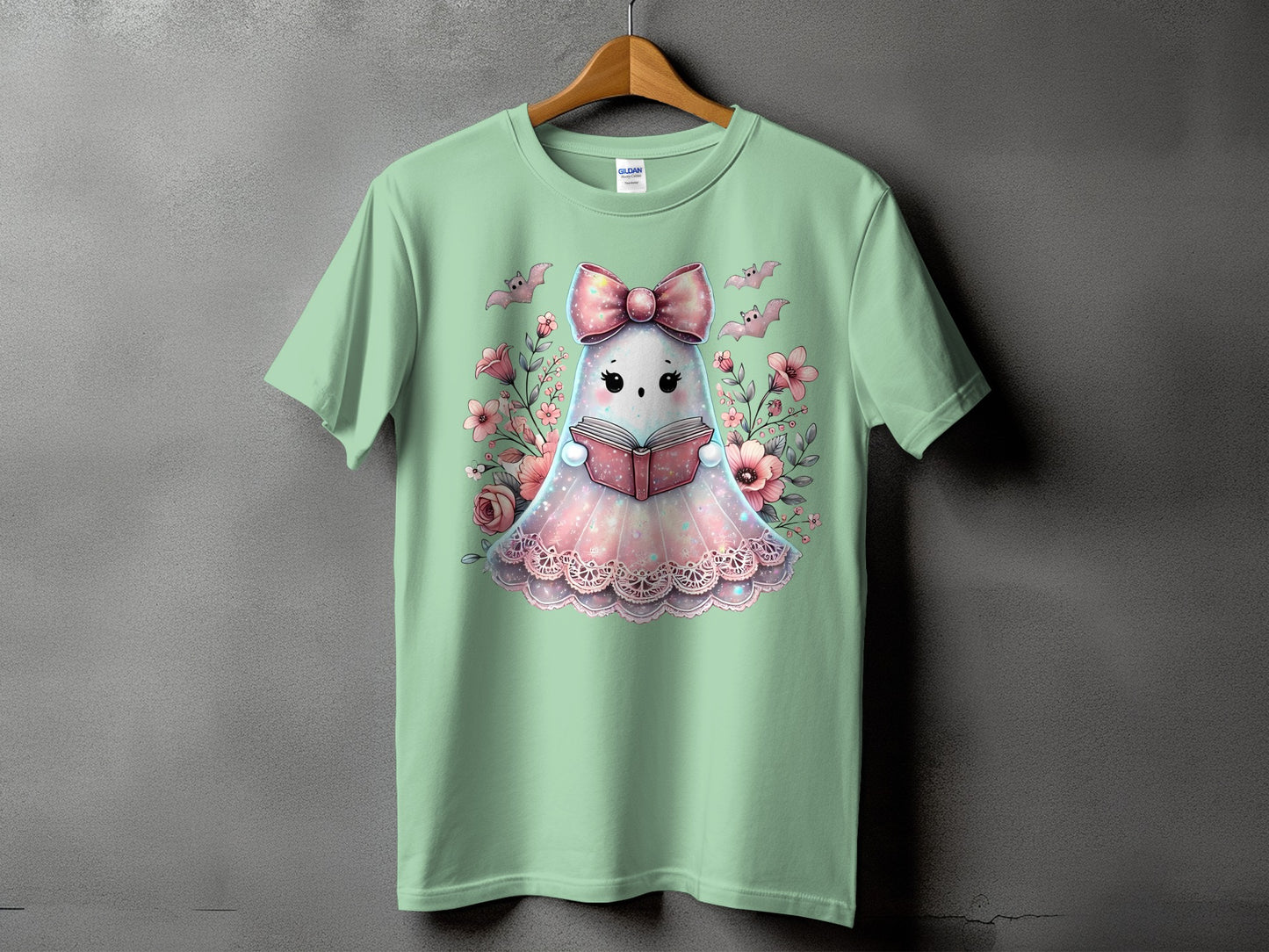 Mint green t-shirt with a ghost reading a book surrounded by flowers and bats.