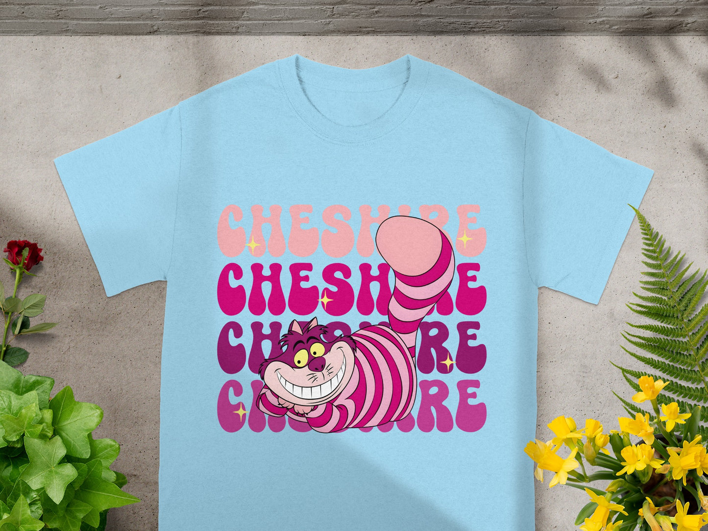 Cheshire Cat graphic with "Cheshire" text in pink and purple on a light blue t-shirt.
