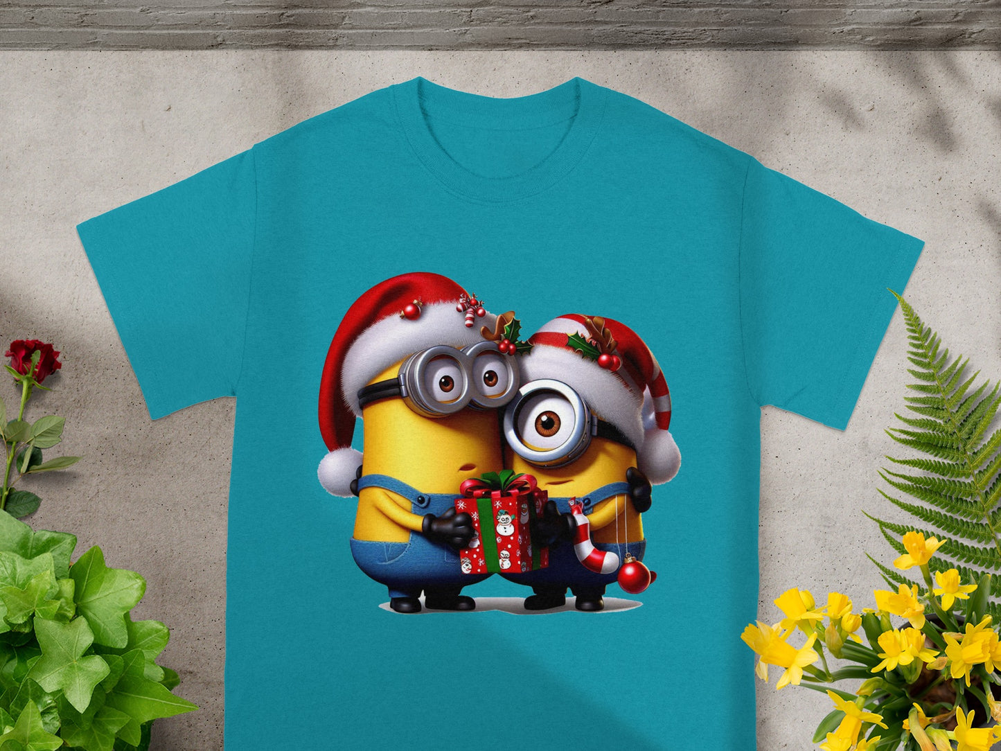 Two minions in Santa hats holding a gift and candy cane, printed on a teal t-shirt.