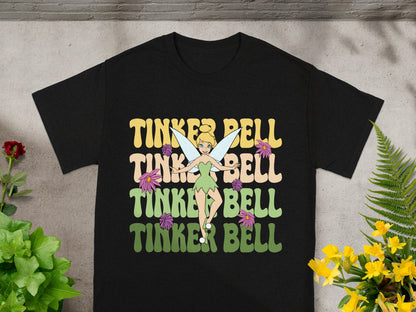 Black t-shirt with "Tinker Bell" in colorful, layered text and fairy illustrations.