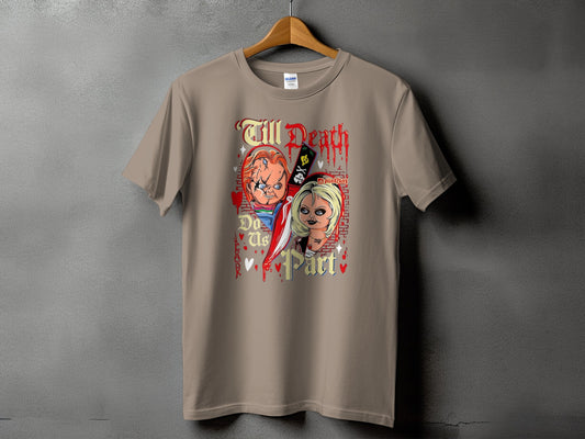 A sandy tan short-sleeve t-shirt featuring a Chucky and Tiffany graphic and text reading "Till Death Do Us Part".