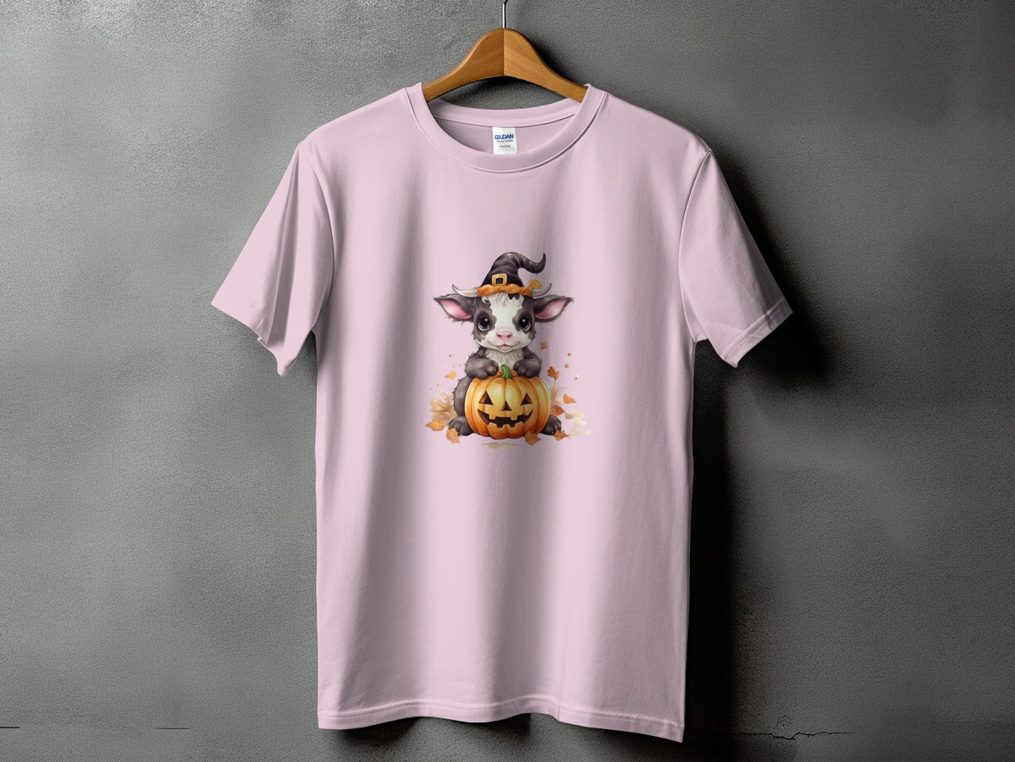 Pink t-shirt with a cow wearing a witch hat on a pumpkin graphic.