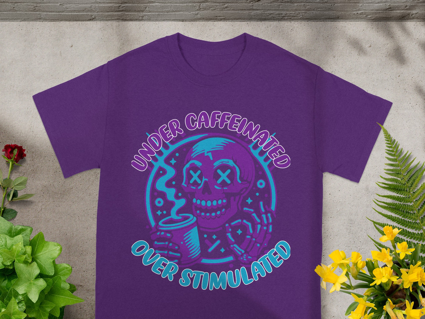 Purple t-shirt with text "UNDER CAFFEINATED OVER STIMULATED" and skeleton graphics.