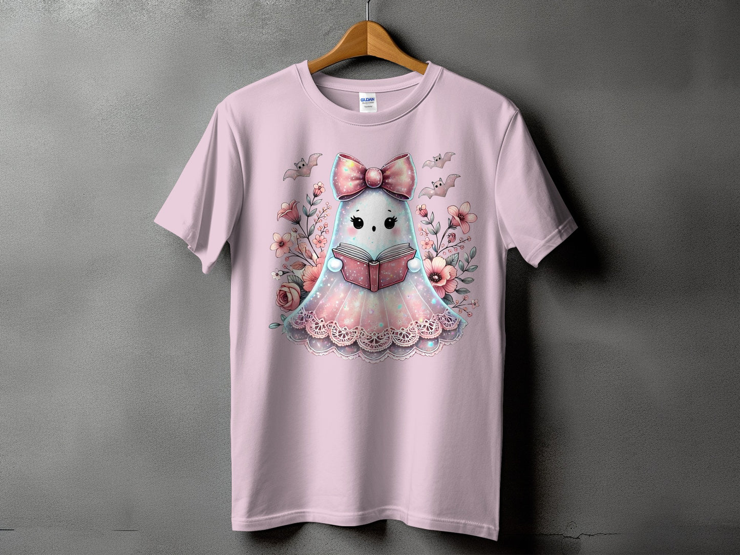 Pink t-shirt with a cute ghost character reading a book surrounded by flowers and bats.