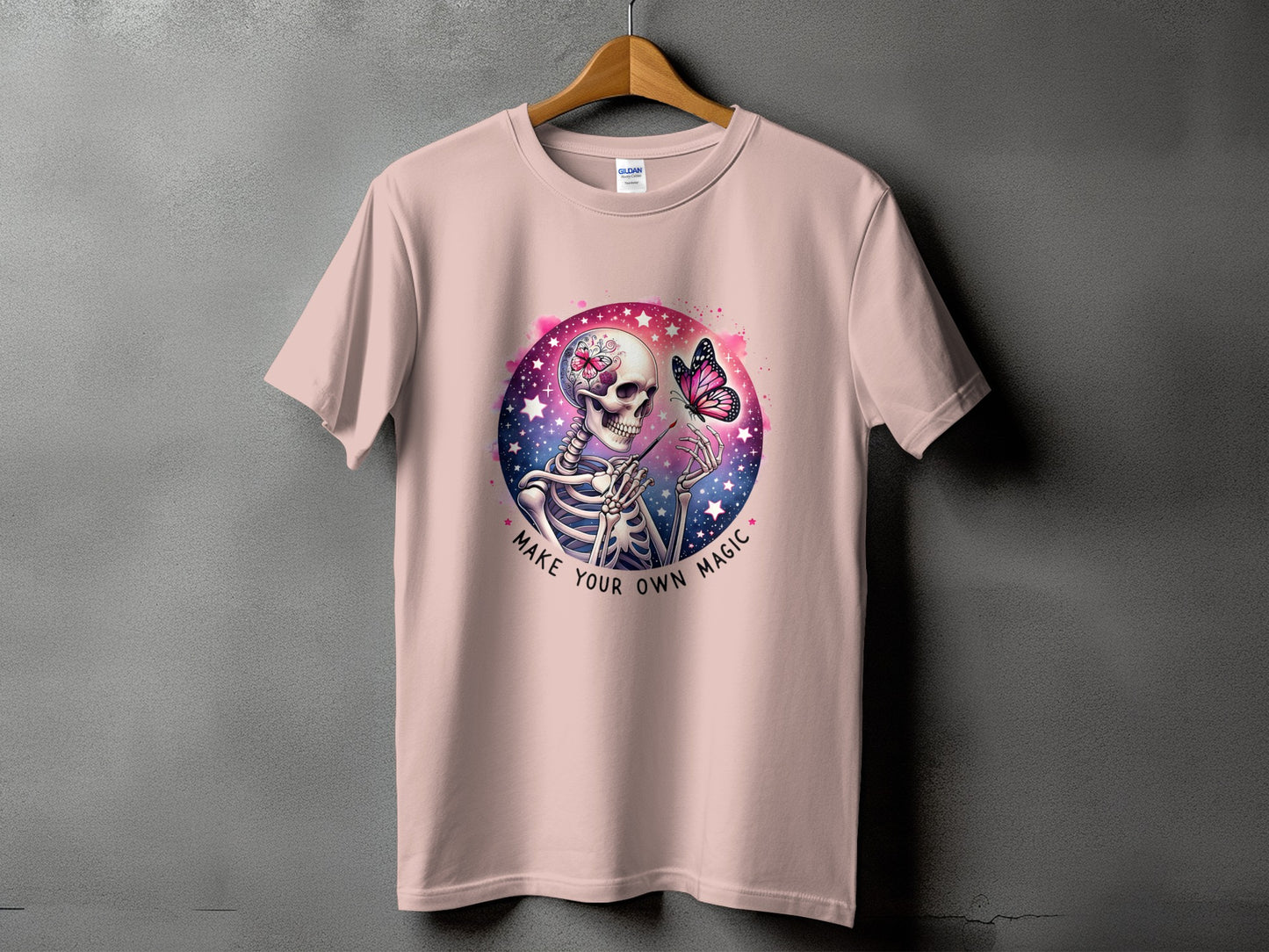 Pink t-shirt with skeleton and butterfly graphic that reads "Make Your Own Magic".