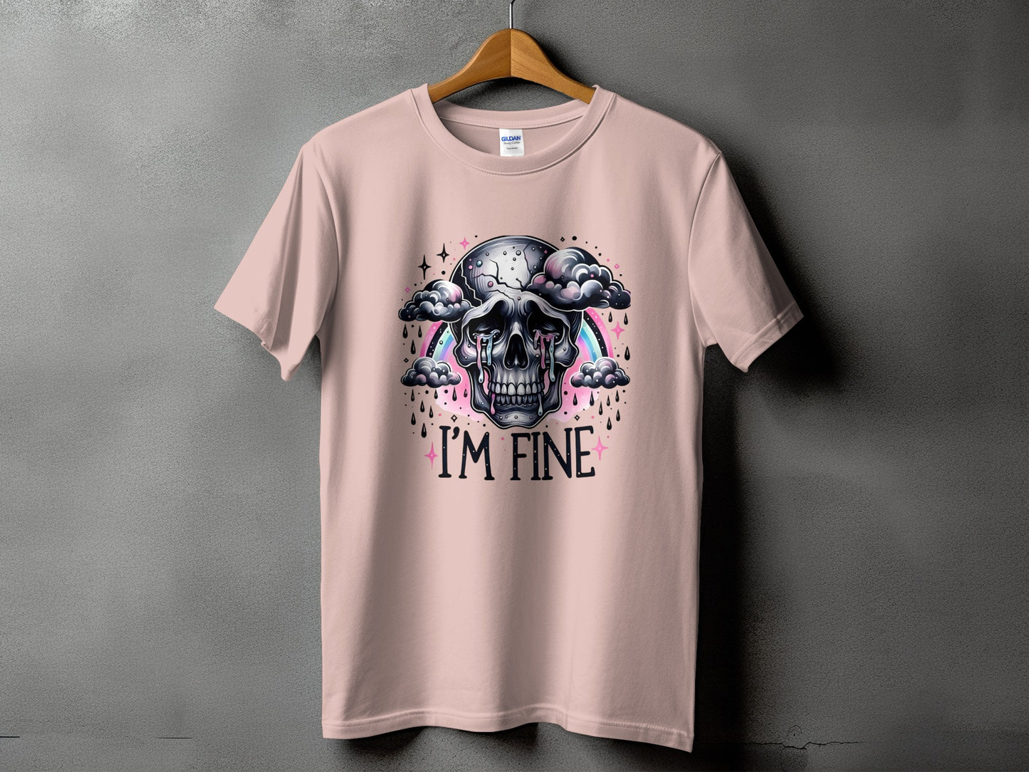 Pink t-shirt with skull graphic crying under a rainbow and clouds, text "I'M FINE".
