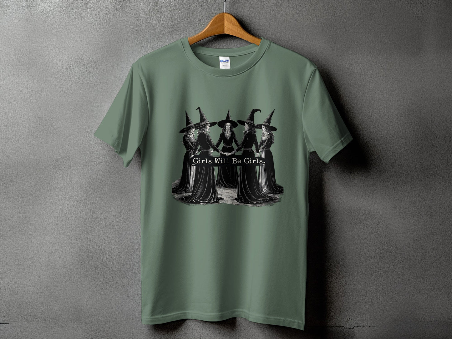 Green t-shirt with a graphic of witches holding hands and text "Girls Will Be Girls".