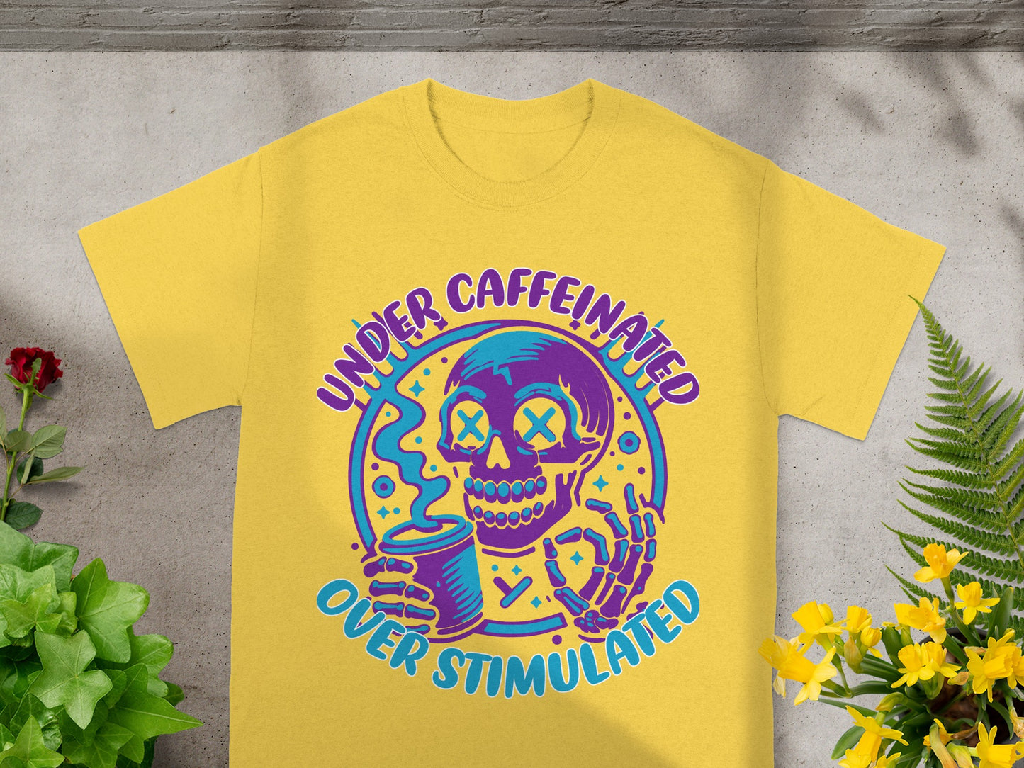 Yellow t-shirt with graphic of skull holding coffee cup and text "UNDER CAFFEINATED OVER STIMULATED".